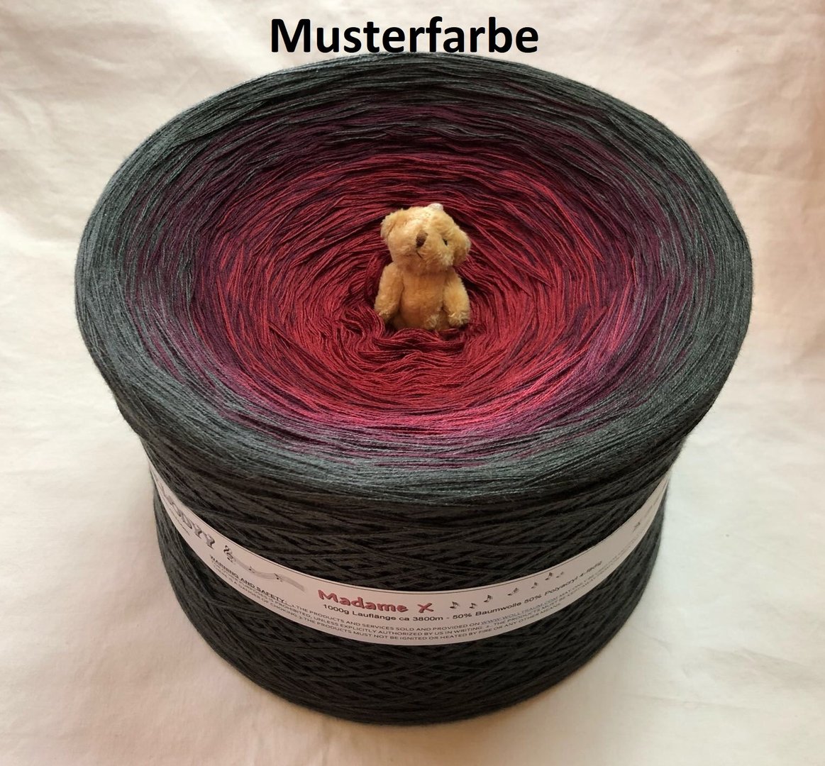 A 1 kilogram Wolltraum yarn cake with red in the middle and black on the outside.  There is a small bear in the middle of the cake.