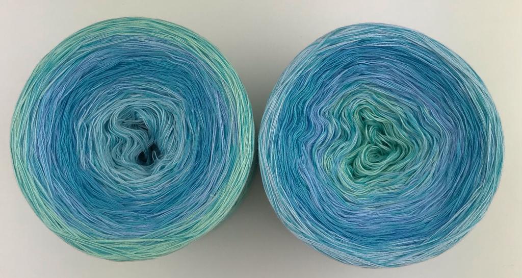 A top view of 2 cakes of the Wolltraum My Melodyy gradient yarn colourway Blue Lagoon.  It contains mixed light blues and light green.