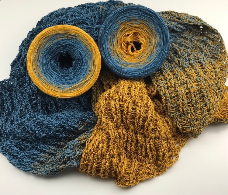 A shawl made with the Wolltraum colour Blue Wall.  Two cakes of yarn lie on the shawl.