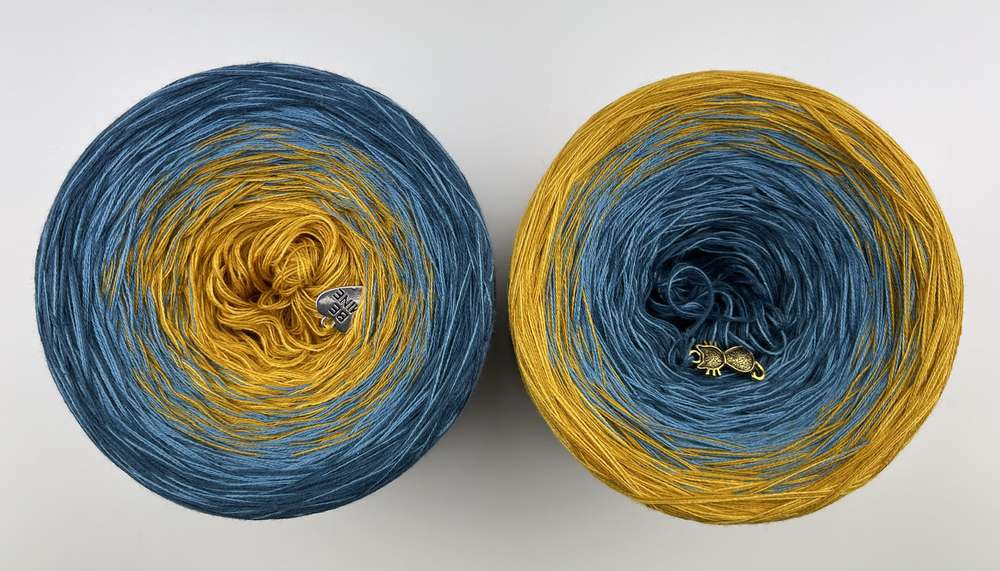 Top view of 2 cakes of the Wolltraum My Melodyy gradient yarn colourway Blue Wall.  It goes from a dusky blue to curry yellow.