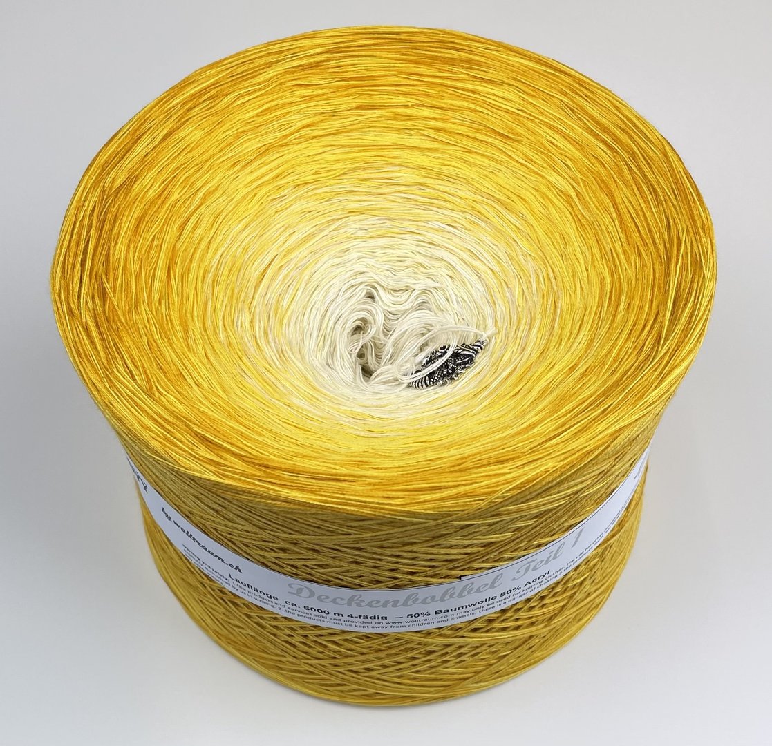 A large cake of Wolltraum yarn that goes from cream to yellow.